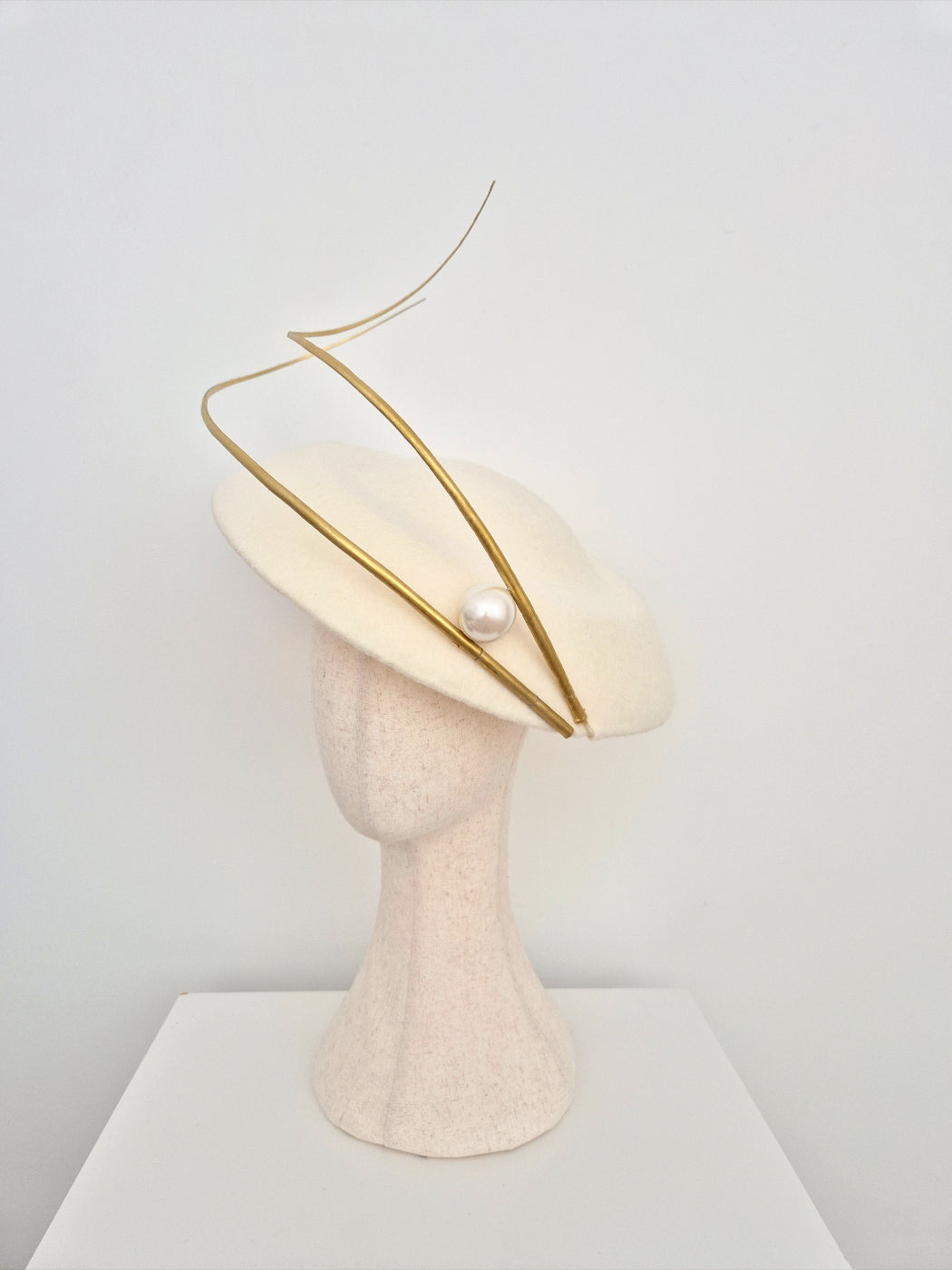 Cream-colored hat with gold accents on a mannequin head against a light gray background side view