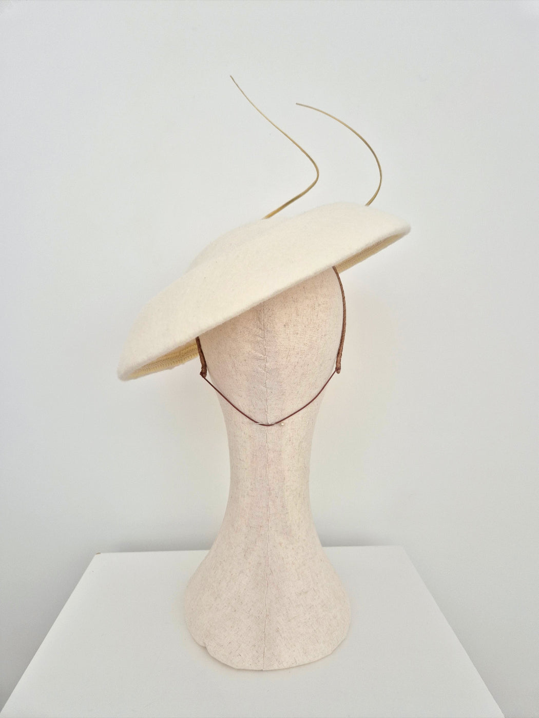 Cream-colored wide-brimmed hat on a mannequin head against a white background back view
