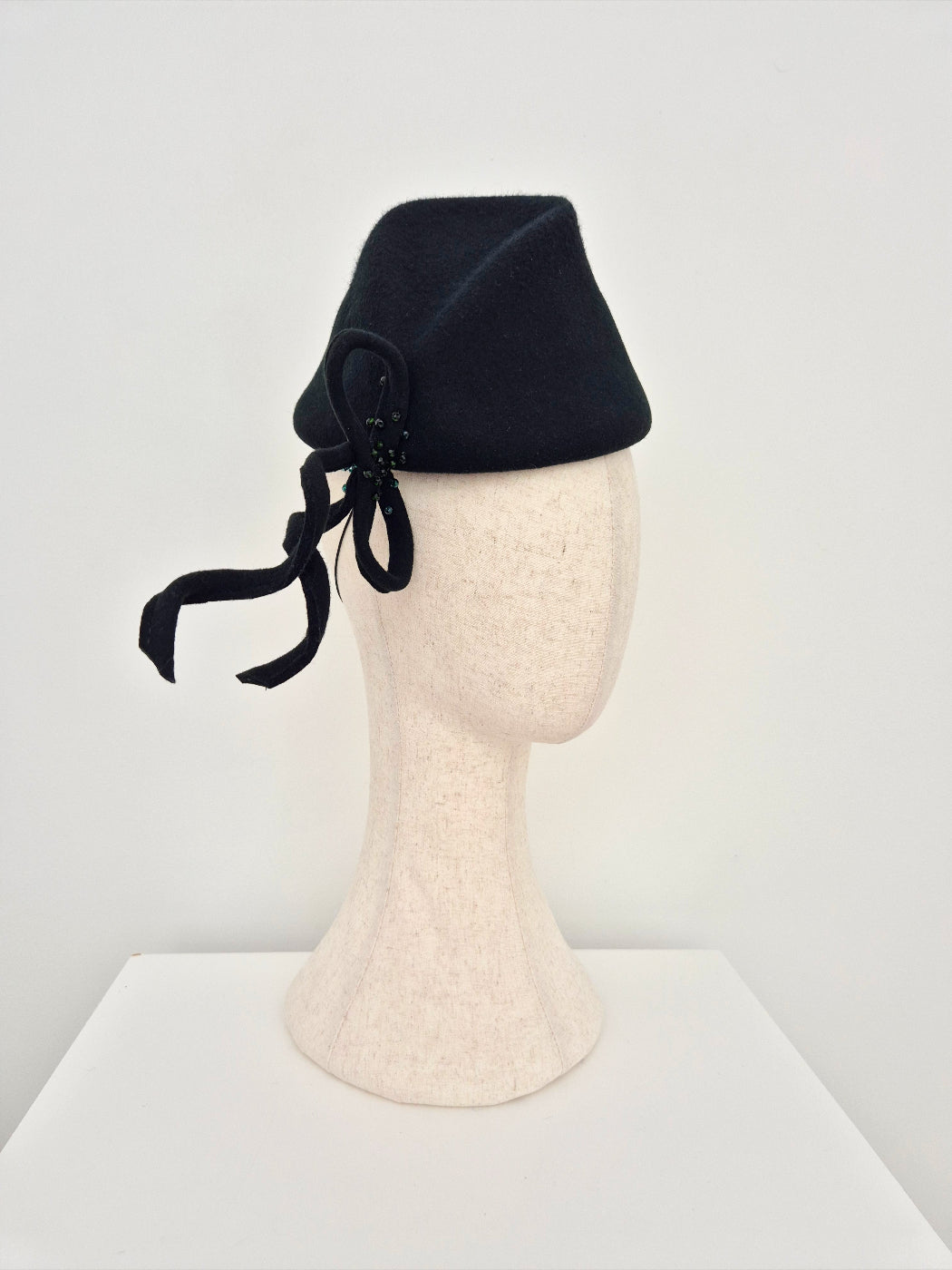dark forest green felted hat  with bow on a mannequin head against a white background side view