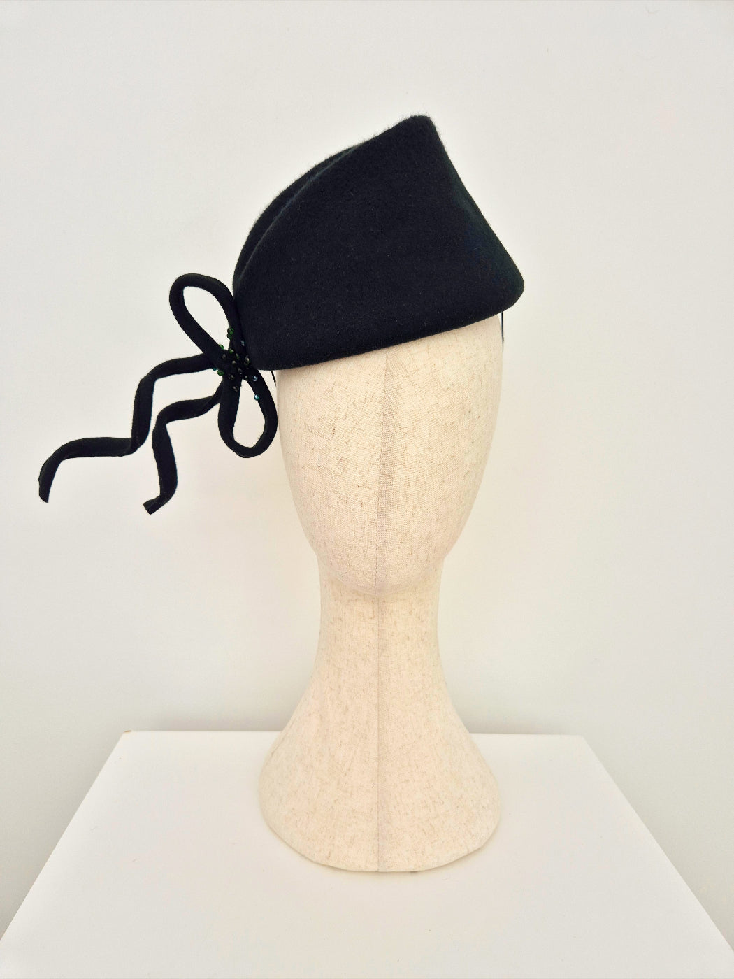 dark forest green headpiece with a bow on a mannequin head against a white background