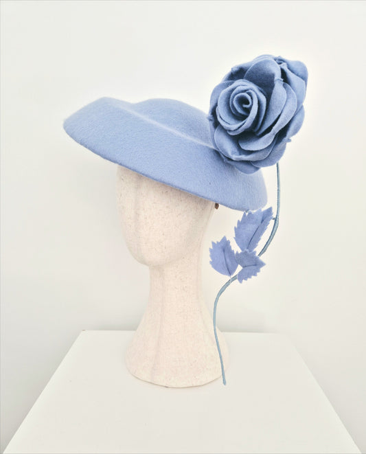 dusty blue felt  hat with a large flower on a mannequin head against a white background side view