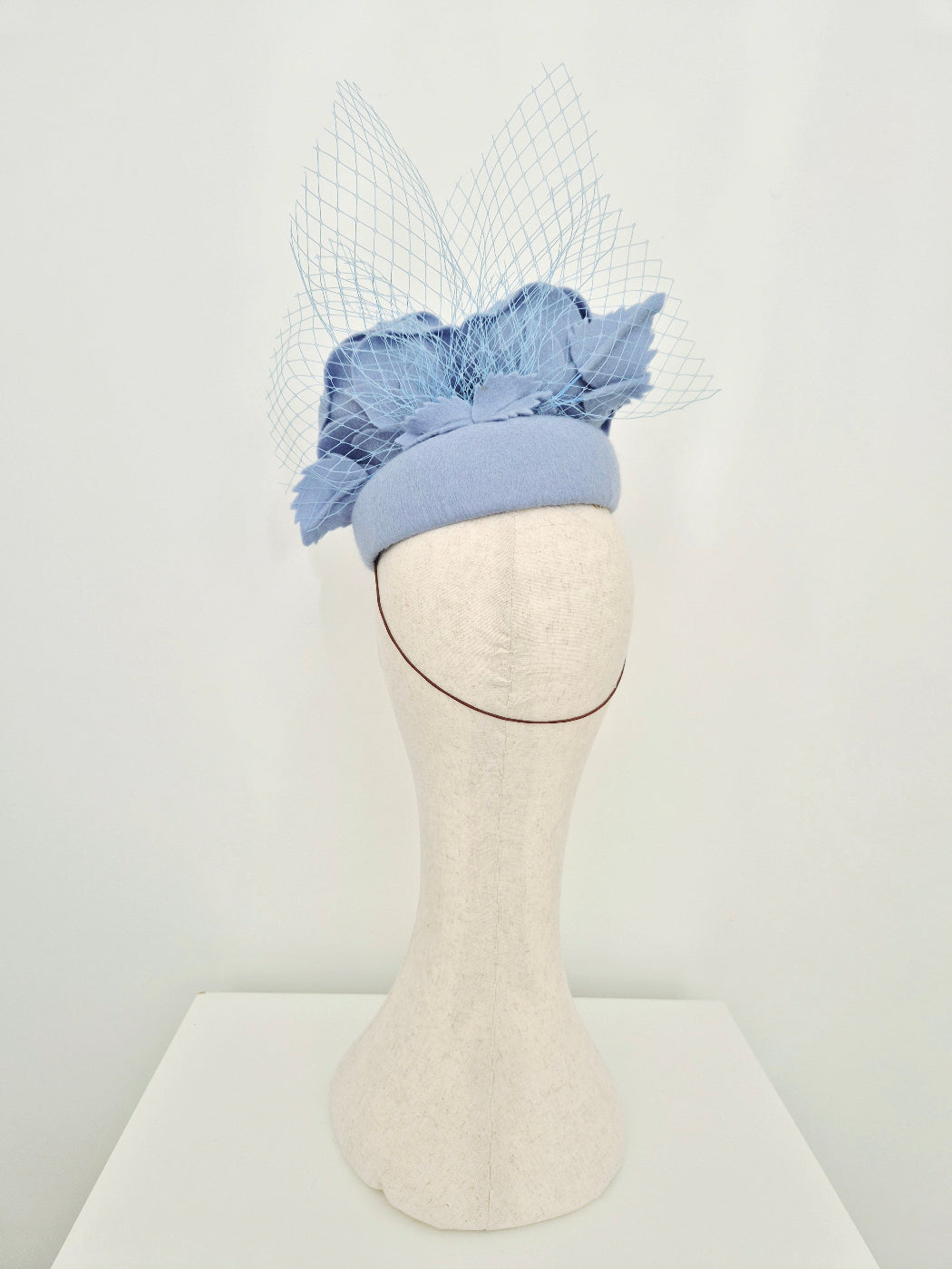 Blue felt  headpiece with rose and veiling mannequin head against a white background back view