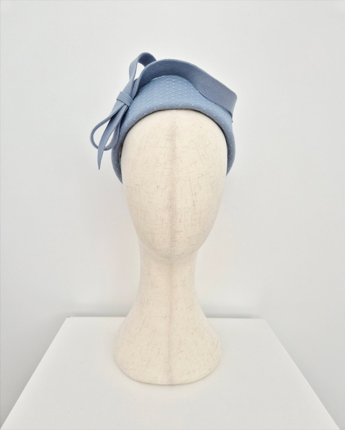 Dusty blue pillbox headpiece on a mannequin head against a white background