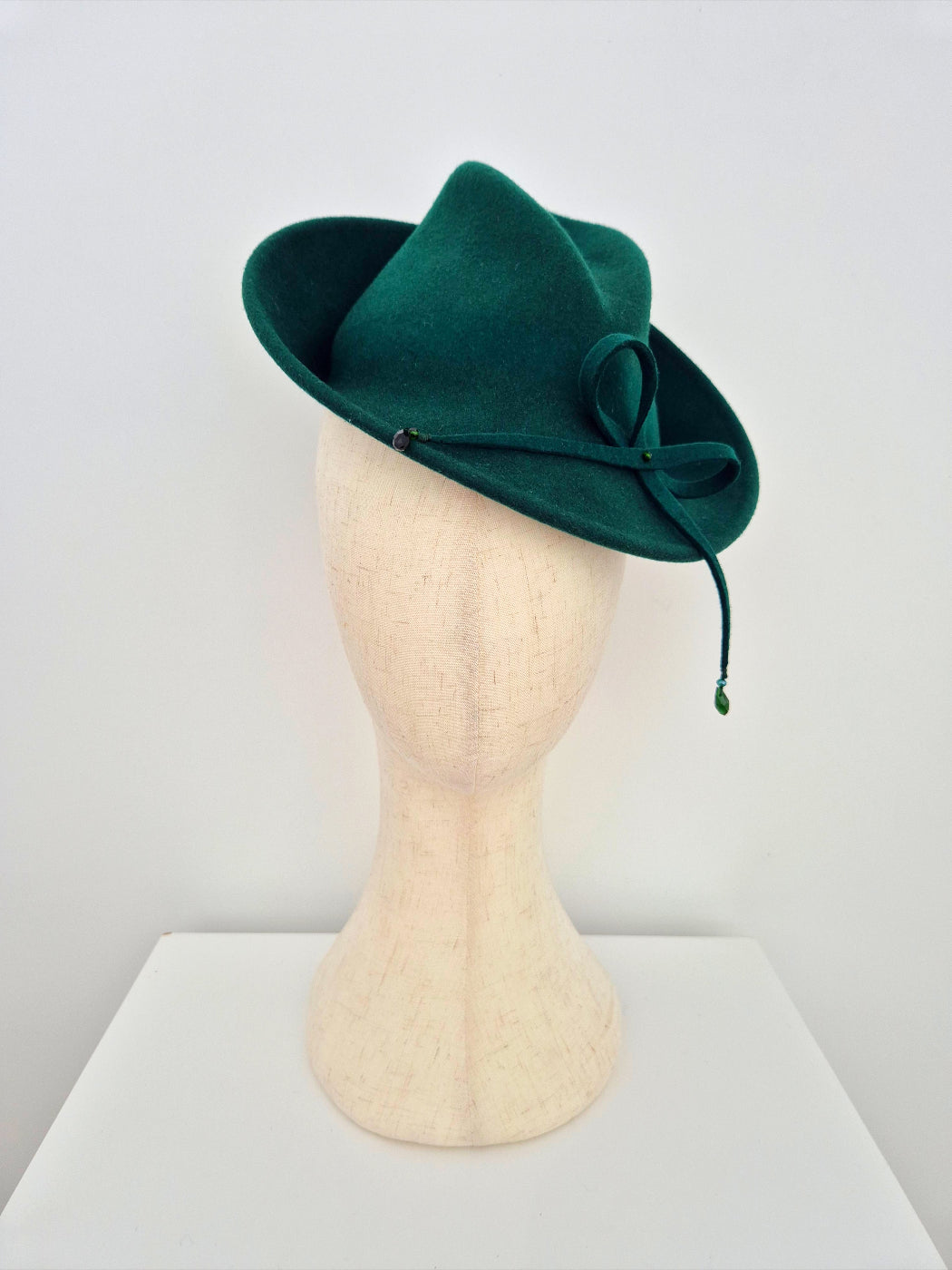 Green felt hat on a mannequin head against a white background