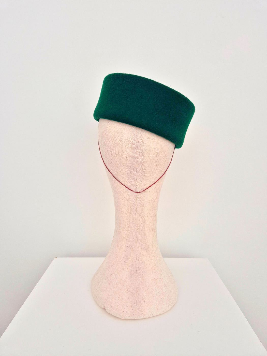 Green pillbox headpiece on a mannequin head against a white background back view