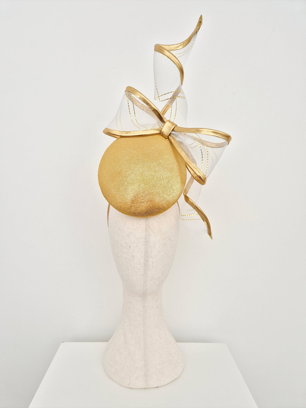 Gold headpiece with a large bow on a mannequin head against a white background