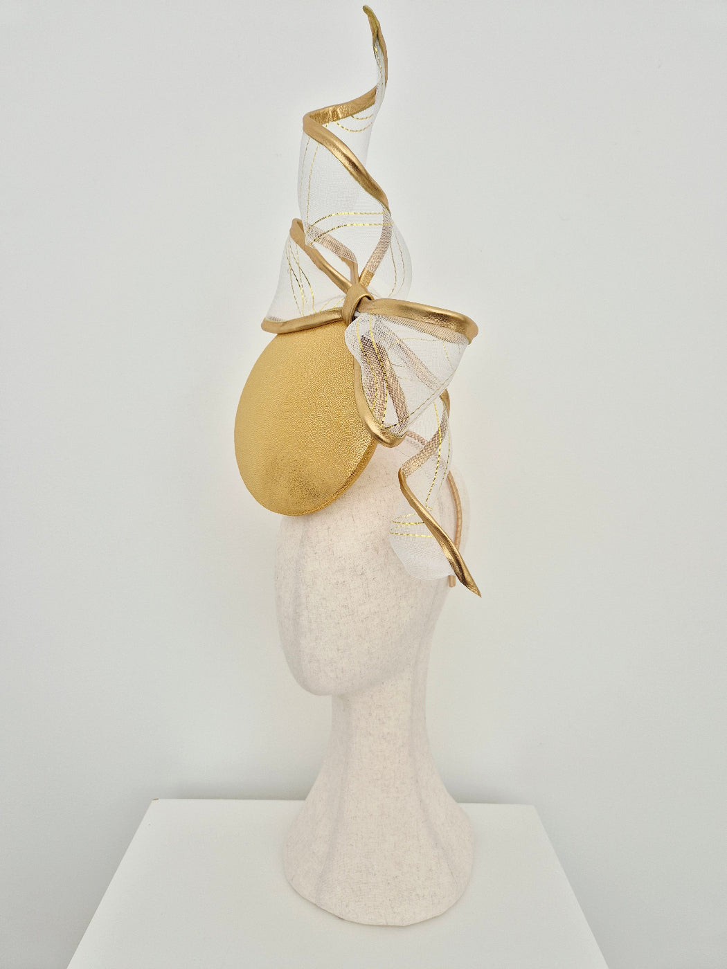 gold button percher millinery with bow and tails on a manniquin head against a white background side view