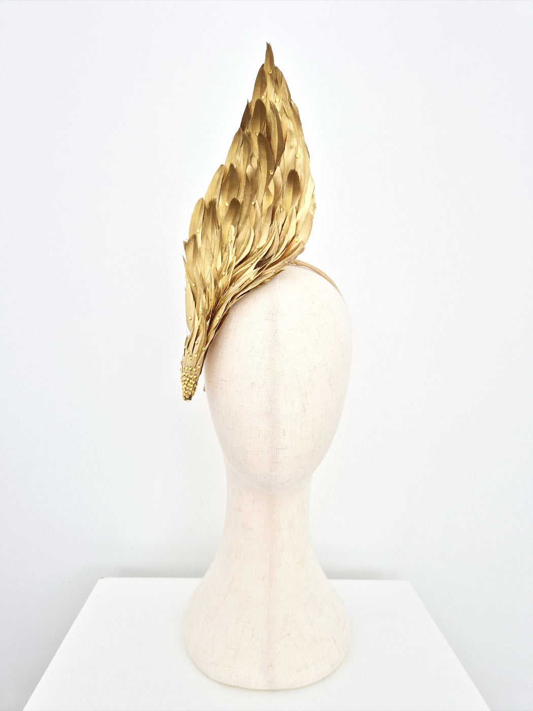 Gold feather headpiece on a mannequin head against a white background