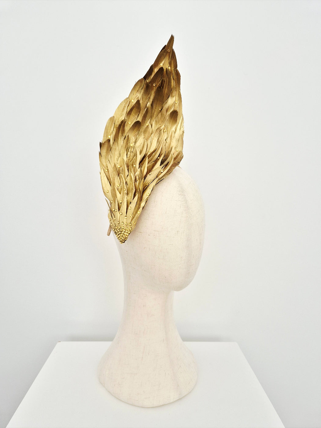 Gold feather headpiece on a mannequin head against a white background side view