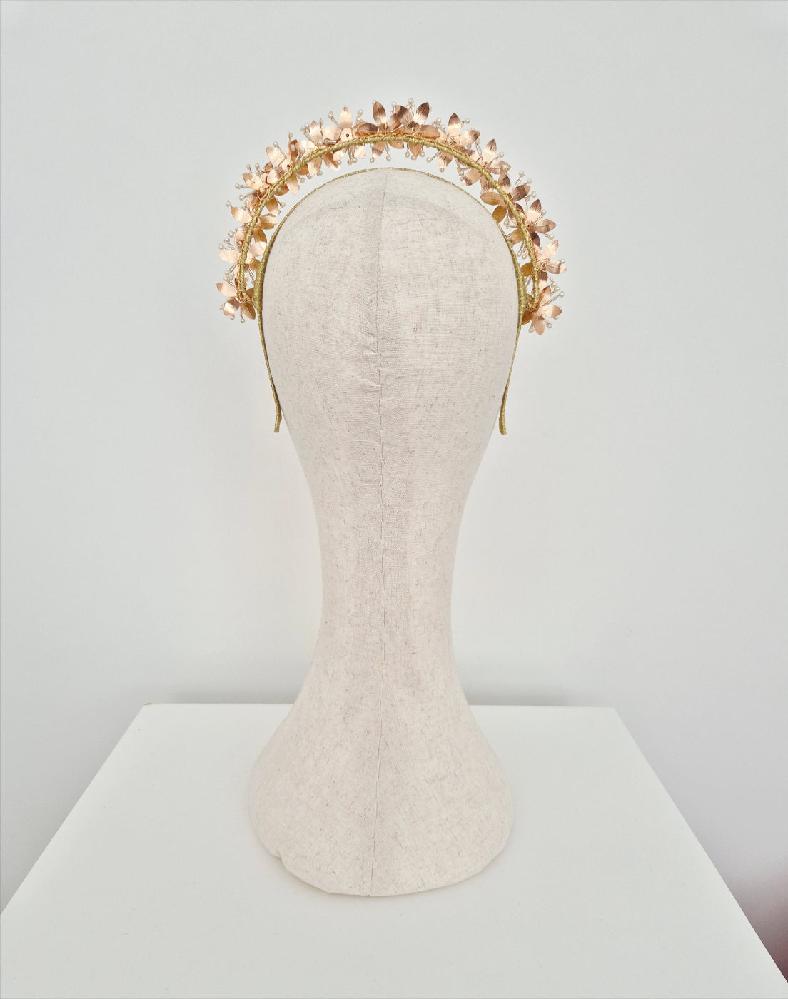 Gold floral headband on a mannequin head against a plain background back view