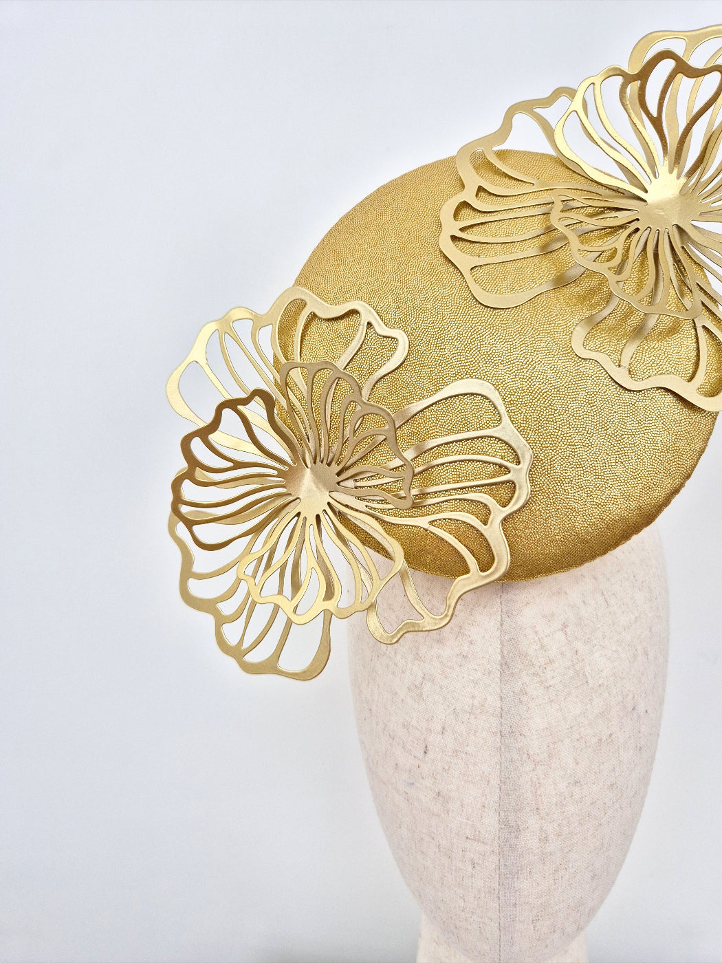 Gold headpiece with floral designs on a mannequin head against a light gray background close up