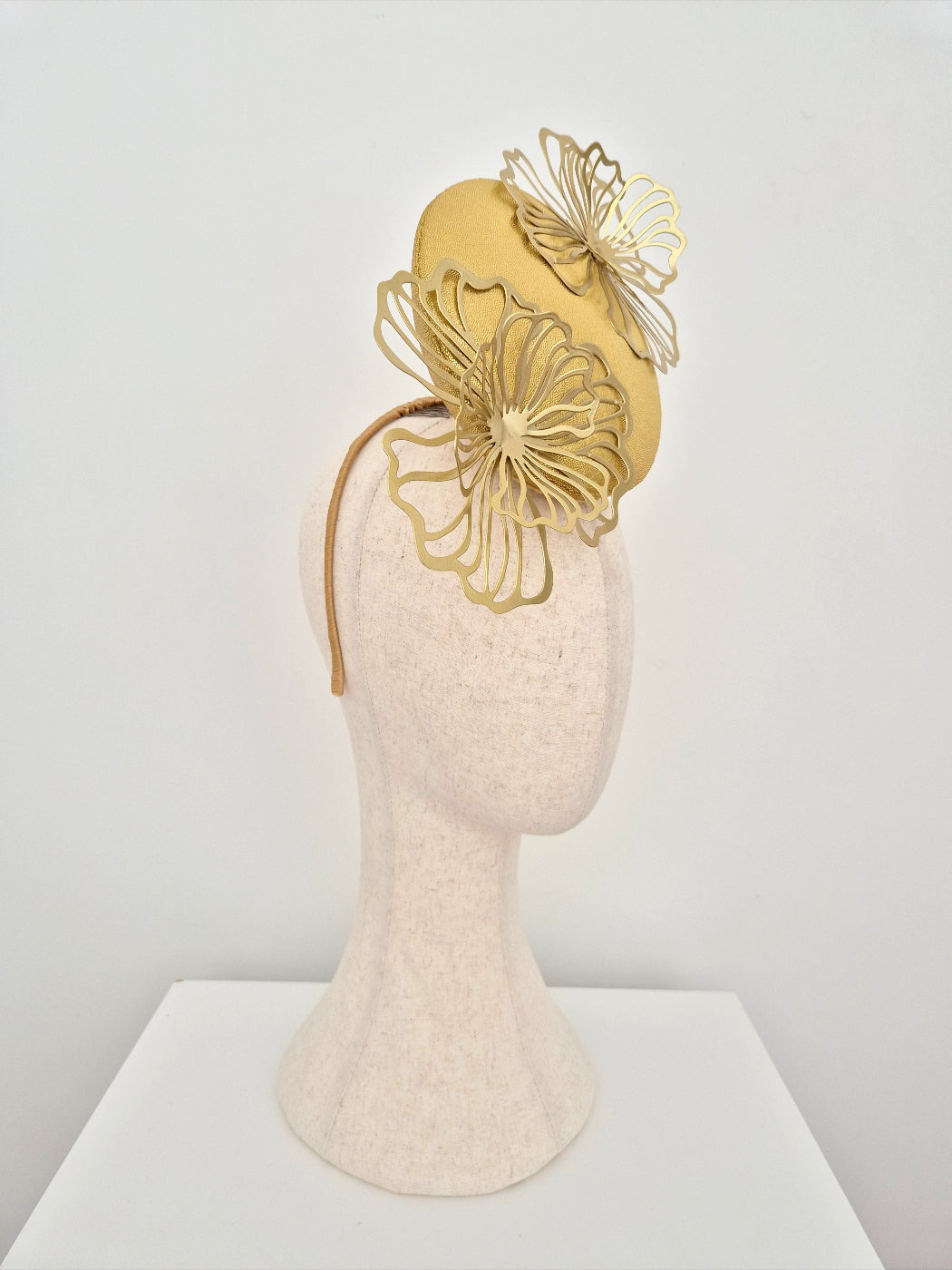 Gold headpiece on a mannequin head against a white background with flowers side view