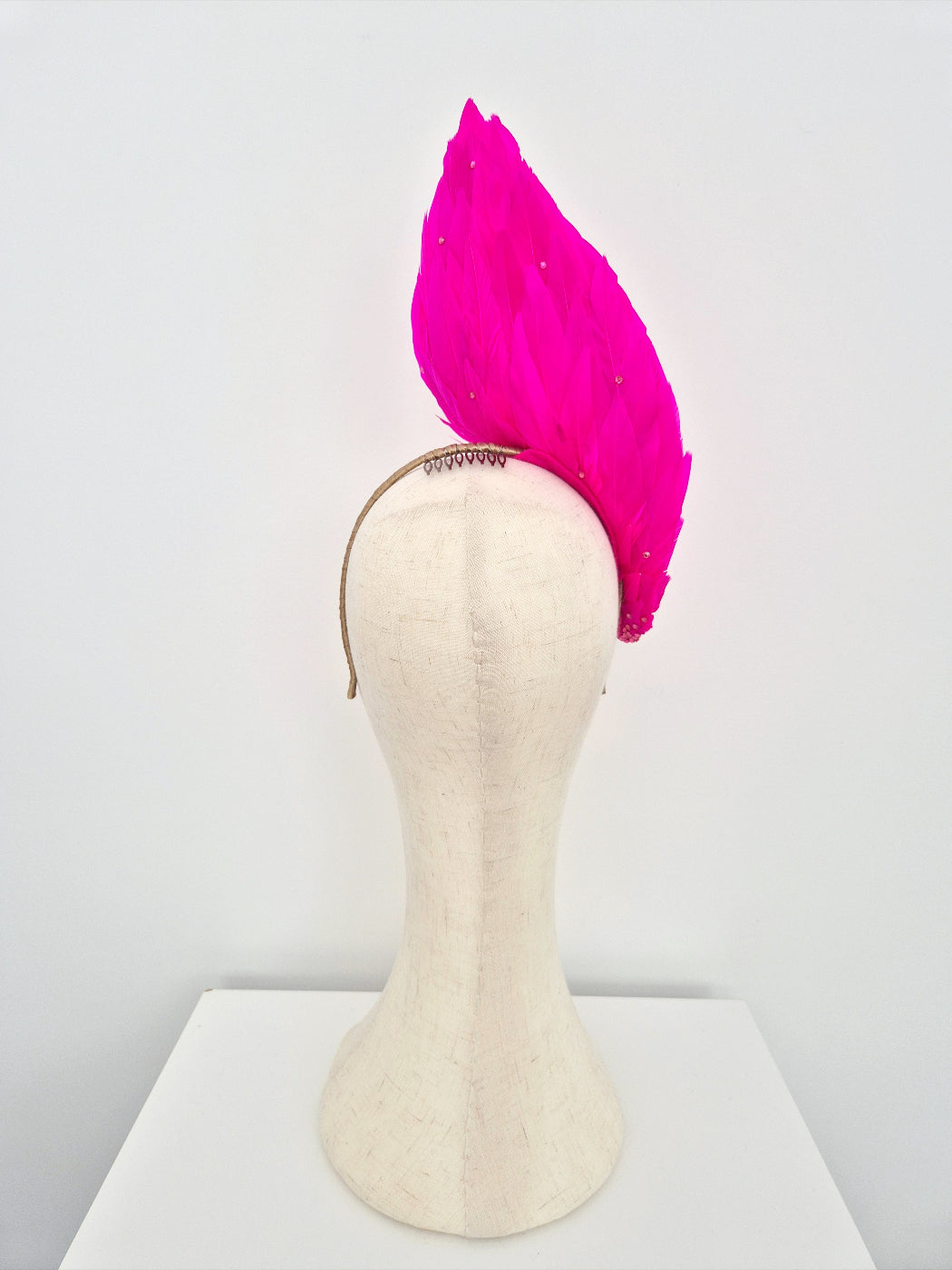 Mannequin head with a hot pink feather headpiece on a white background back view