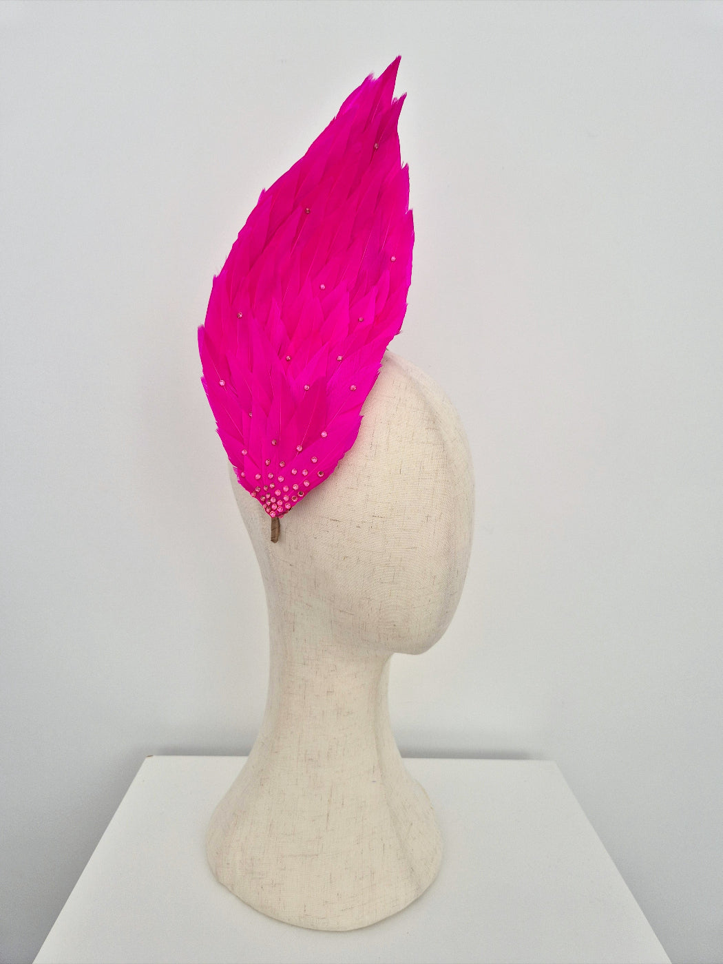 Pink feathered headpiece on a mannequin head against a white background side view