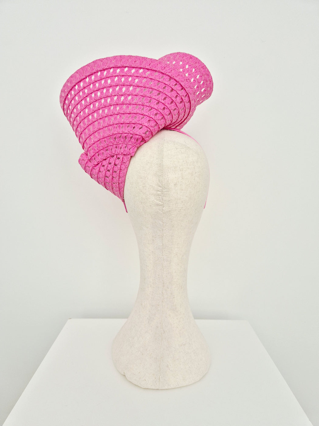 A bright pink woven fascinator hat displayed on a cream-colored mannequin head against a clean white background. back view