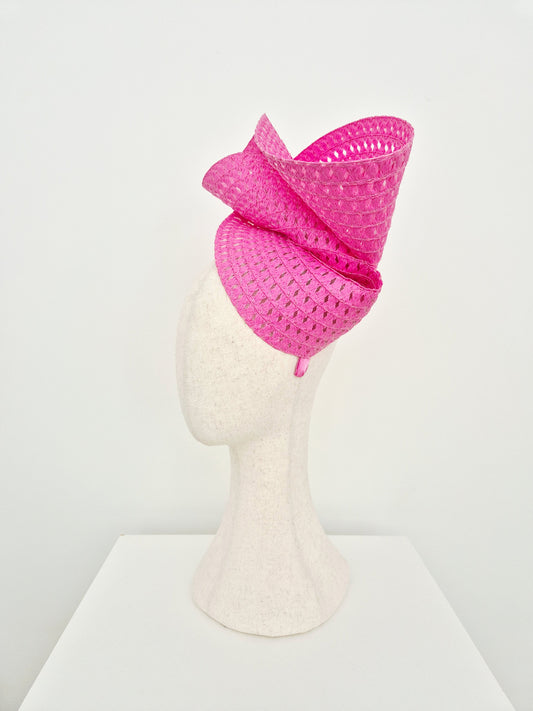 A bright pink woven fascinator hat displayed on a white mannequin head against a clean white background.side view