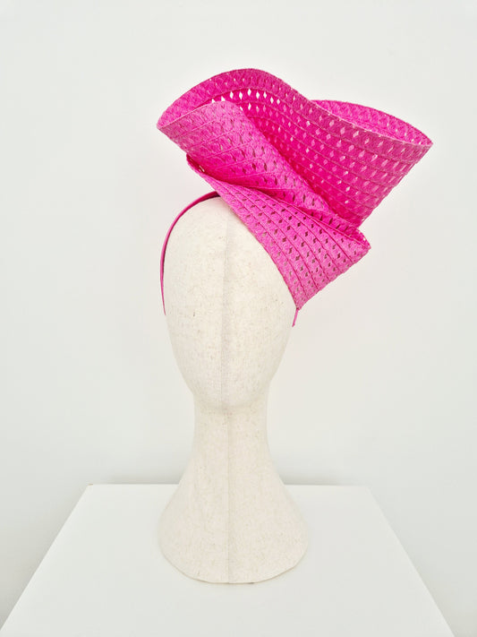 A bright pink woven fascinator hat displayed on a white felt mannequin head against a clean white background.
