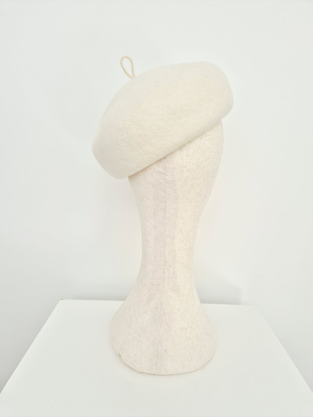 A cream-colored felt beret hat on a  mannequin head against a plain white background. back view