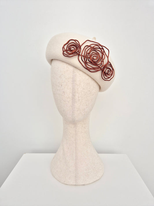 Cream-colored beret with brown floral embellishments on a mannequin head against a white background