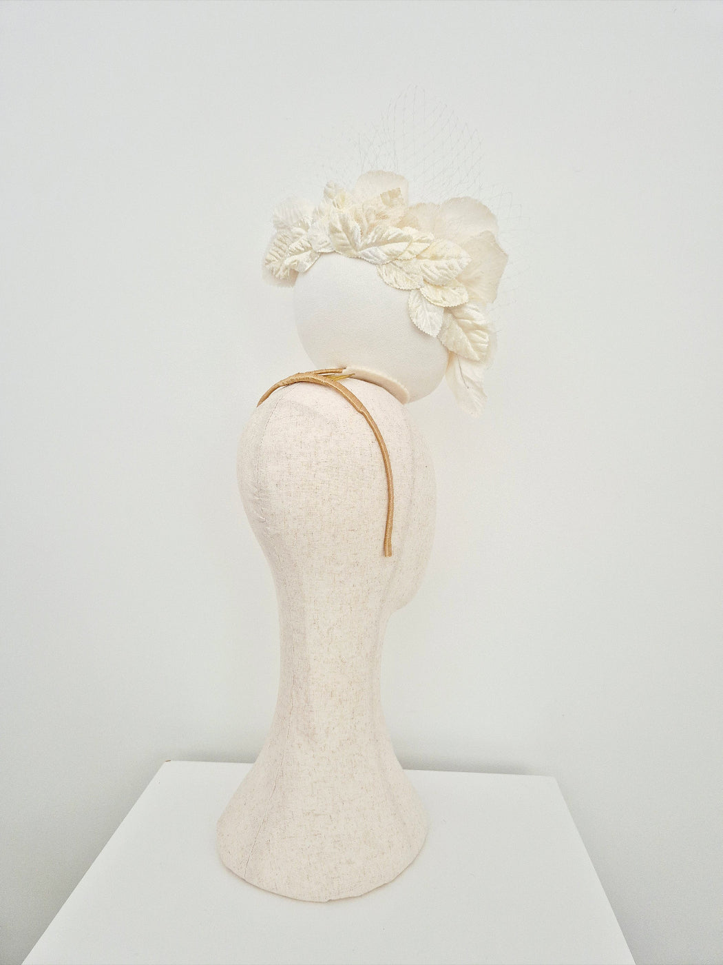 Mannequin head with a ivory floral percher headband on a white background side view