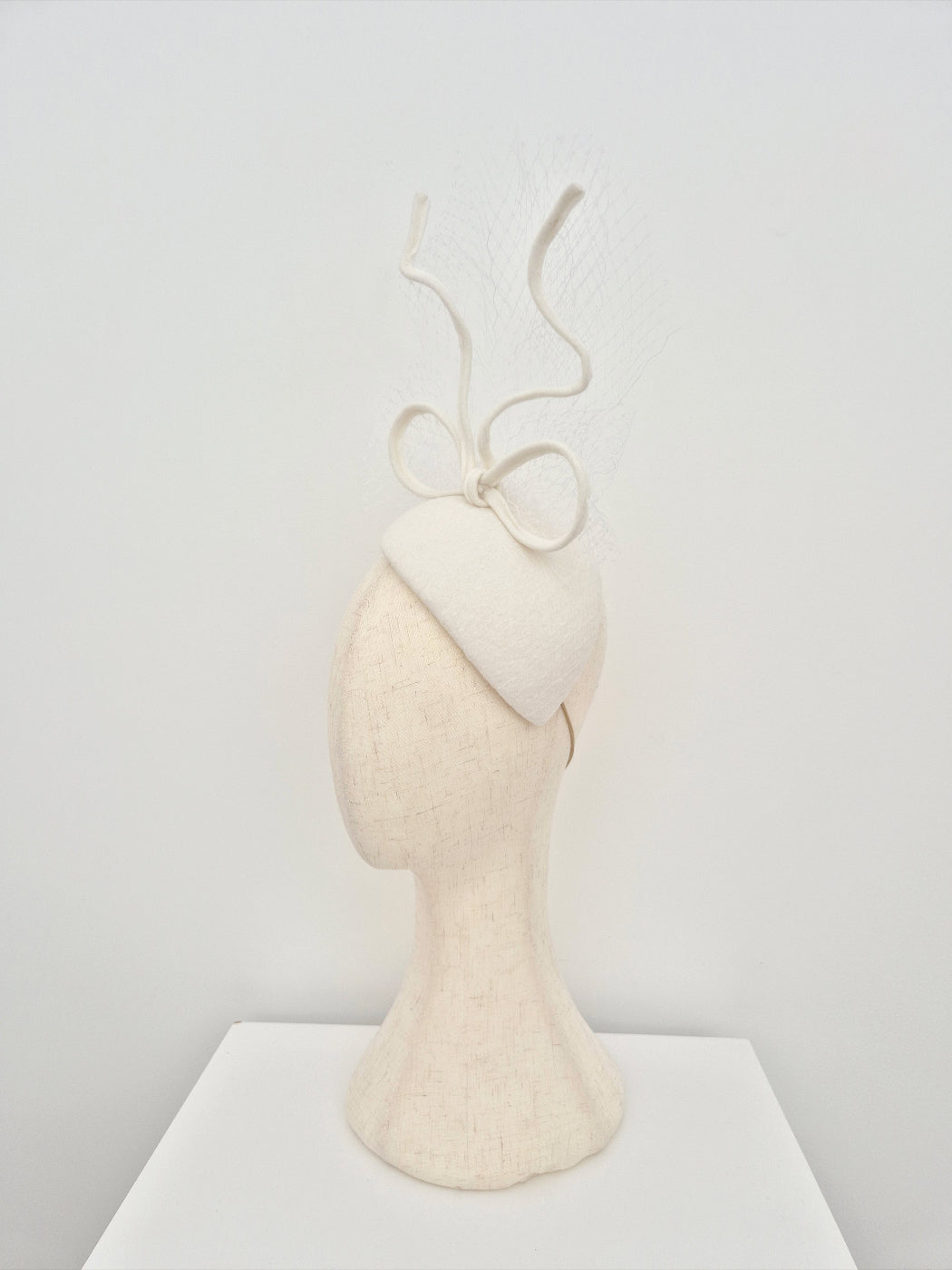 ivory headpiece with a bow on a mannequin head against a plain white background
