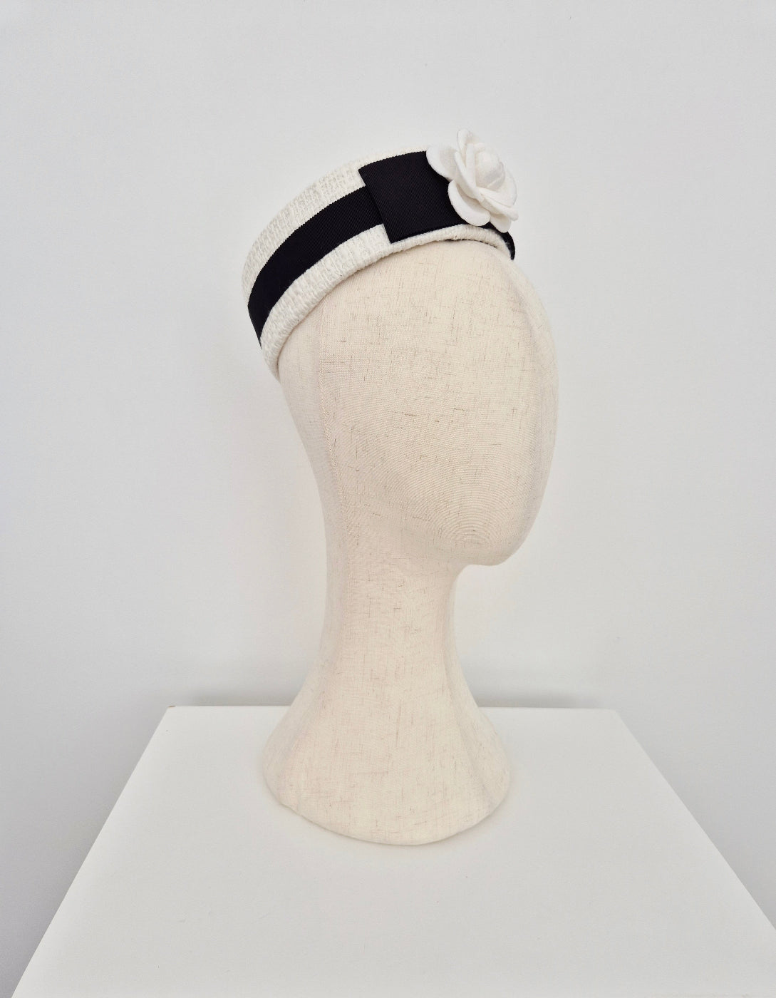 side view ivory tweed pillbox headpiece with a black band and decorative flower on a white background