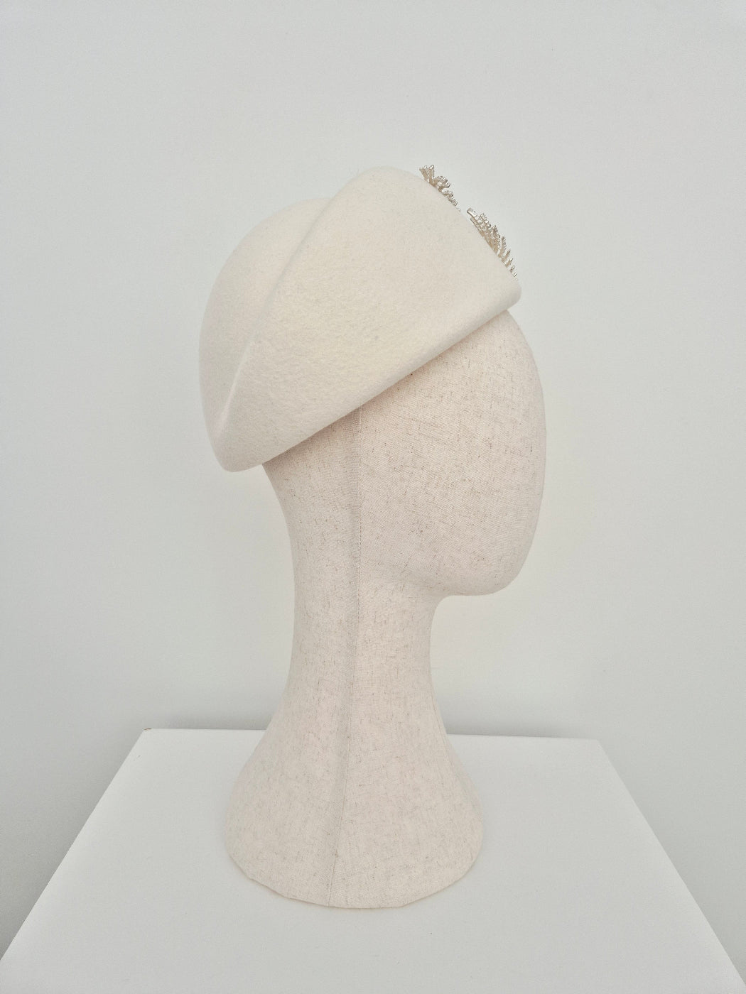 Ivory wool felt beret headpiece with silver fern detail side view on a manniquin head against a white wall