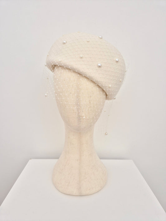 ivory colored wool felt beret with pearl embellishments on a mannequin head against a white background