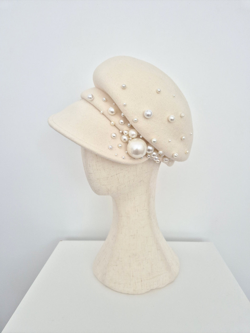 Cream-colored hat with pearl embellishments on a mannequin head against a white background side view