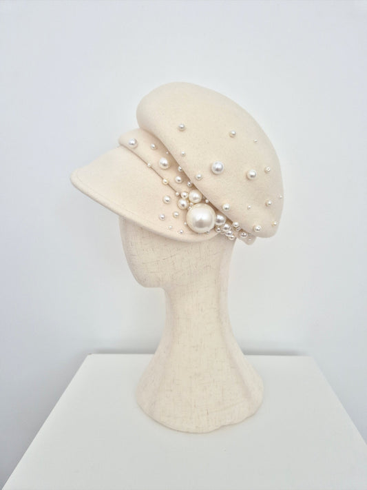 Cream-colored hat with pearl embellishments on a mannequin head against a white background side view