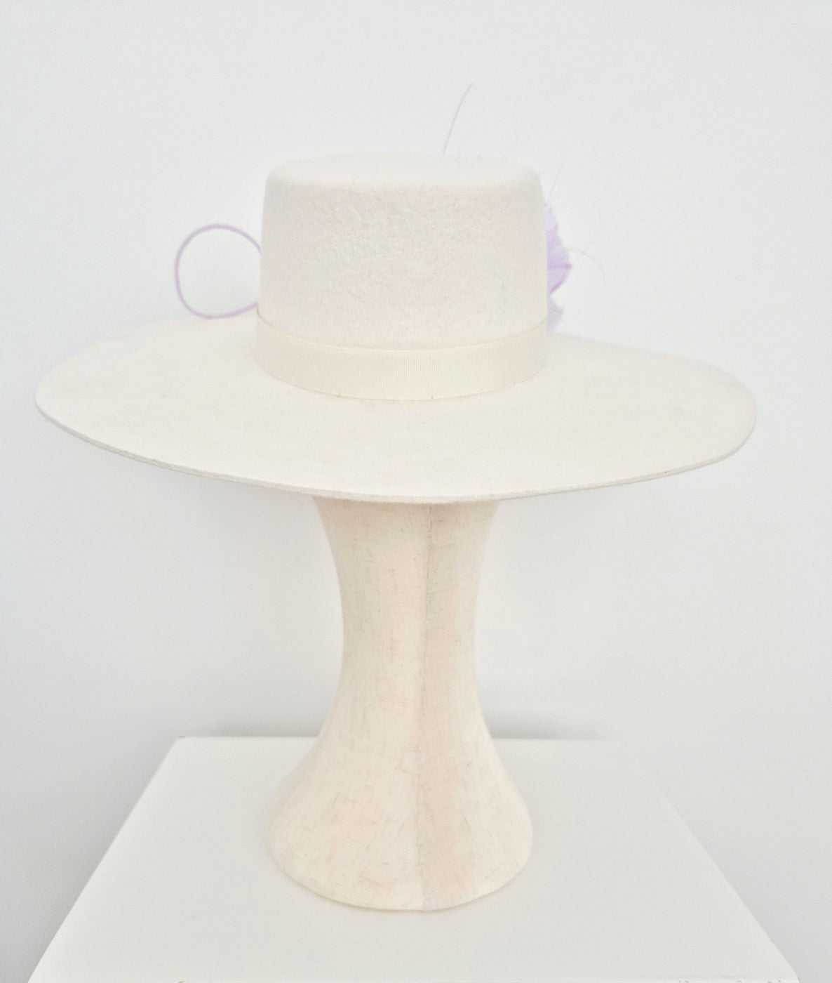 Ivory felt hat on a manniquin head  back view against plain white background 