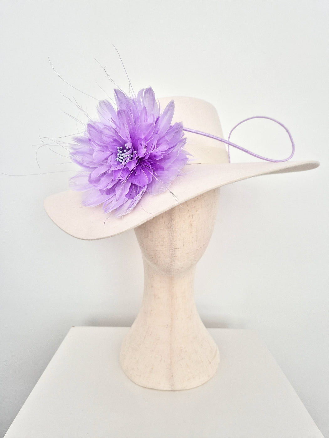 Ivory felt wide-brimmed hat with a purple flower on a mannequin head against a white background