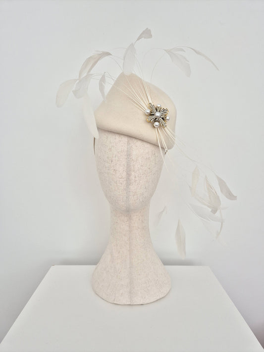 ivory felt headpiece with feathers and brooch detail on a mannequin head against a white background