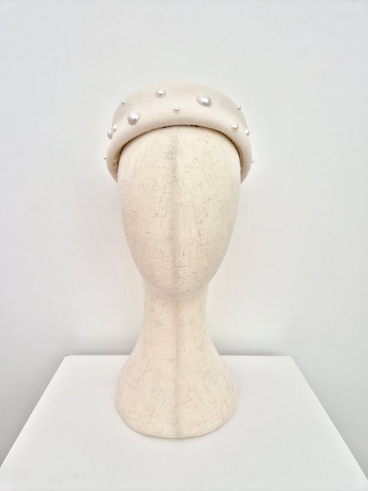 ivory wool felt pillbox headpiece with pearl-like embellishments on a mannequin head against a white background