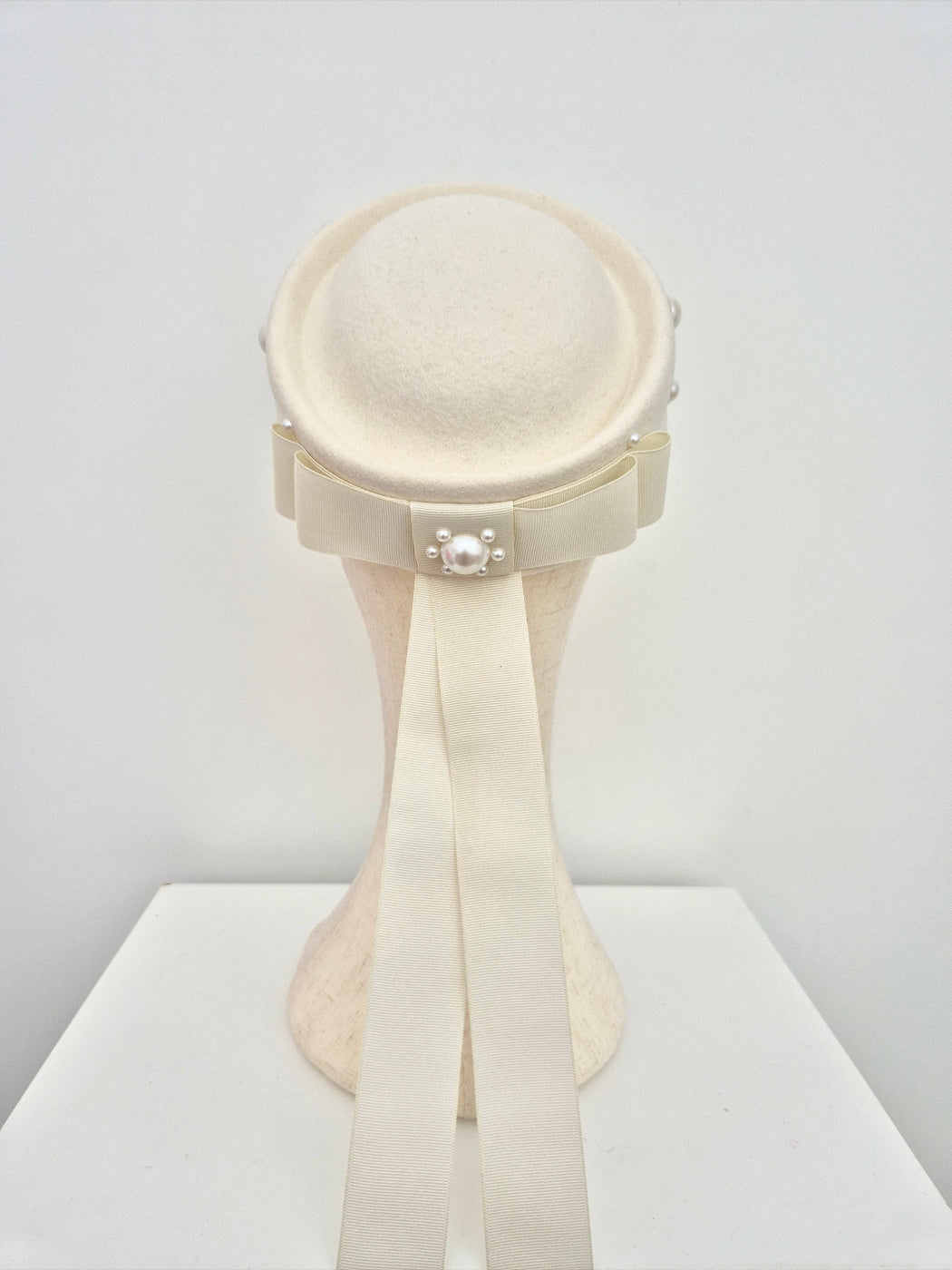 ivory wool felt pillbox headpiece with a bow on a white background back view