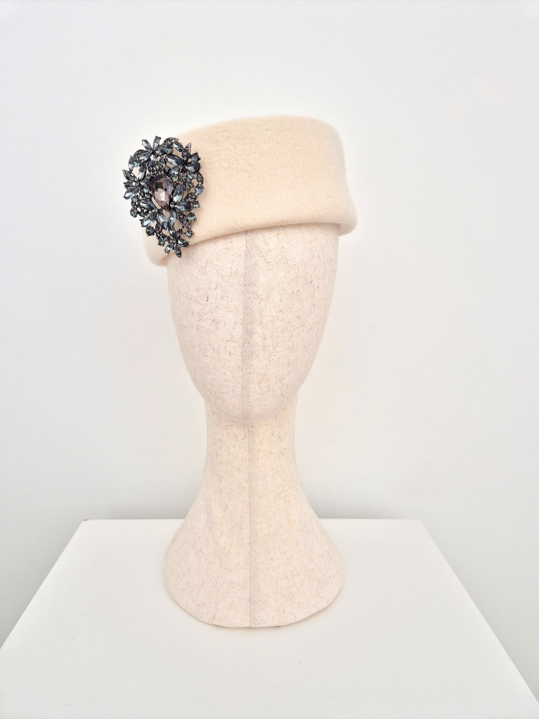 Cream-colored hat with decorative brooch on a mannequin head against a white background
