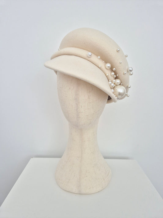 Beige hat with pearl embellishments on a mannequin head against a light gray background