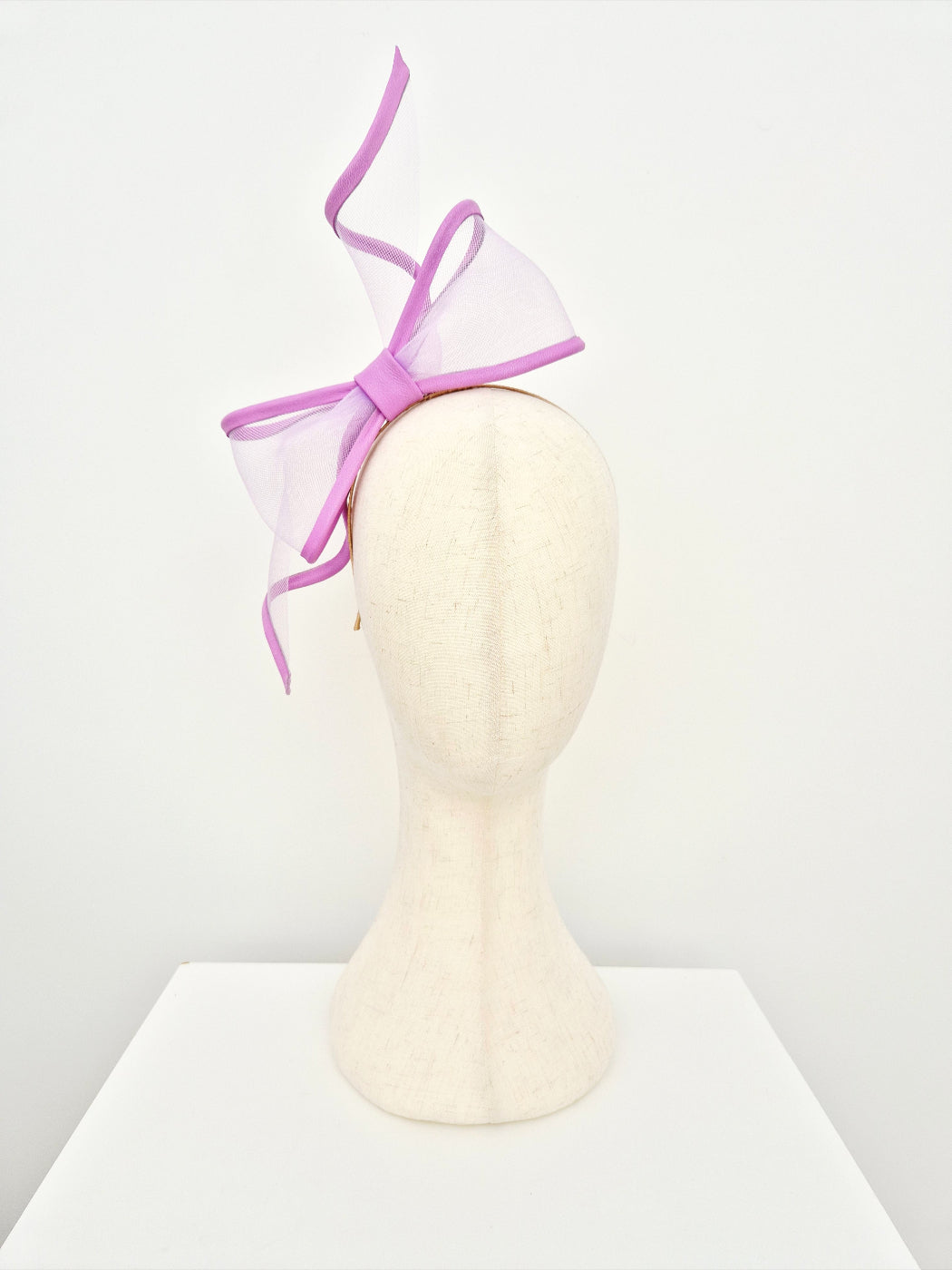 Mannequin head wearing a lavender headband with a sheer bow on a white background