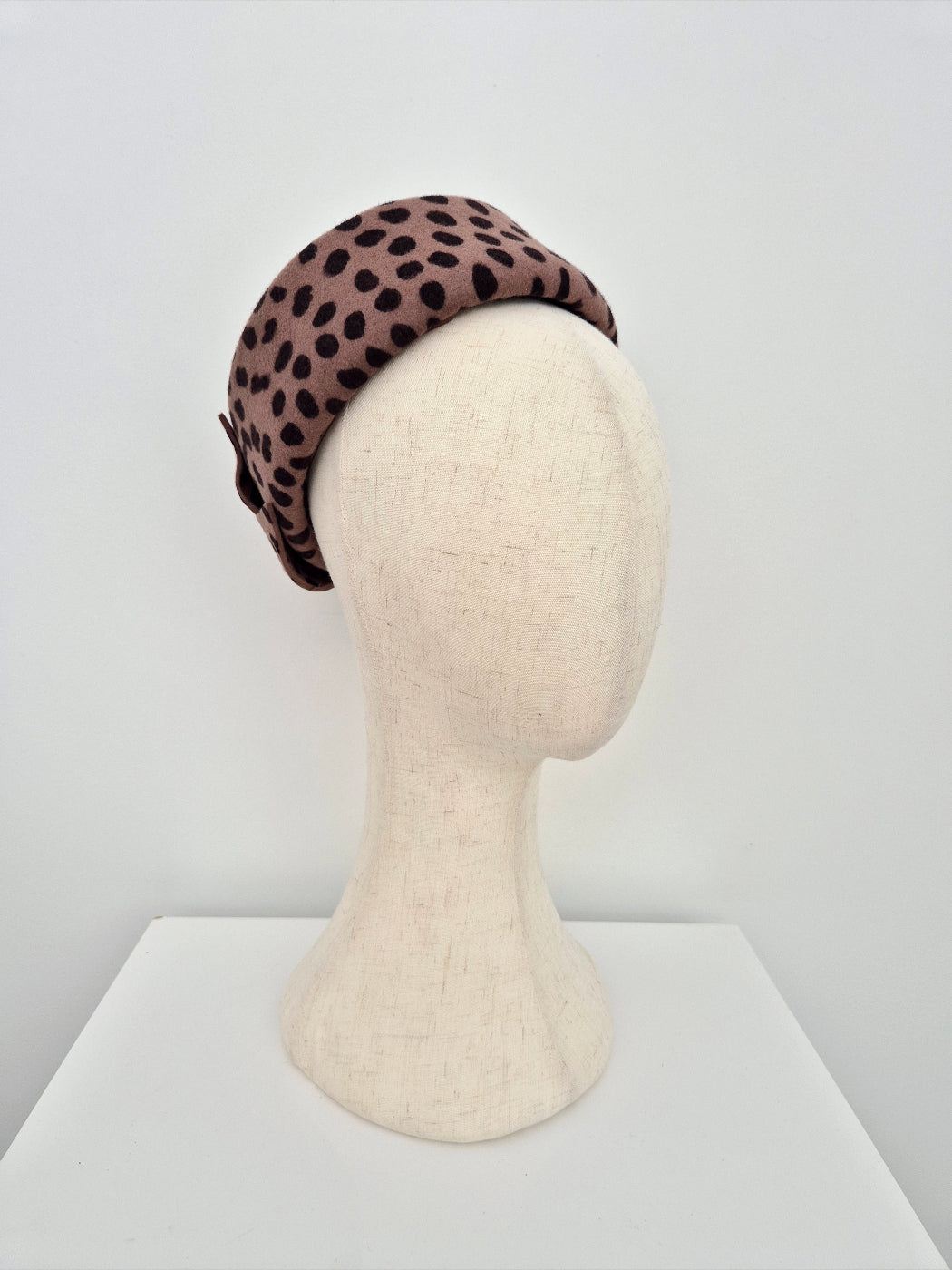 Leopard print pillbox headpiece on a mannequin head against a white background side front