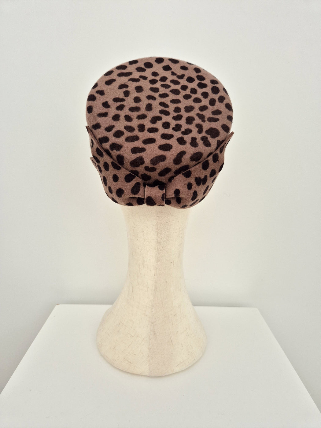 Leopard print pillbox headpiece with bowon a mannequin head against a white background