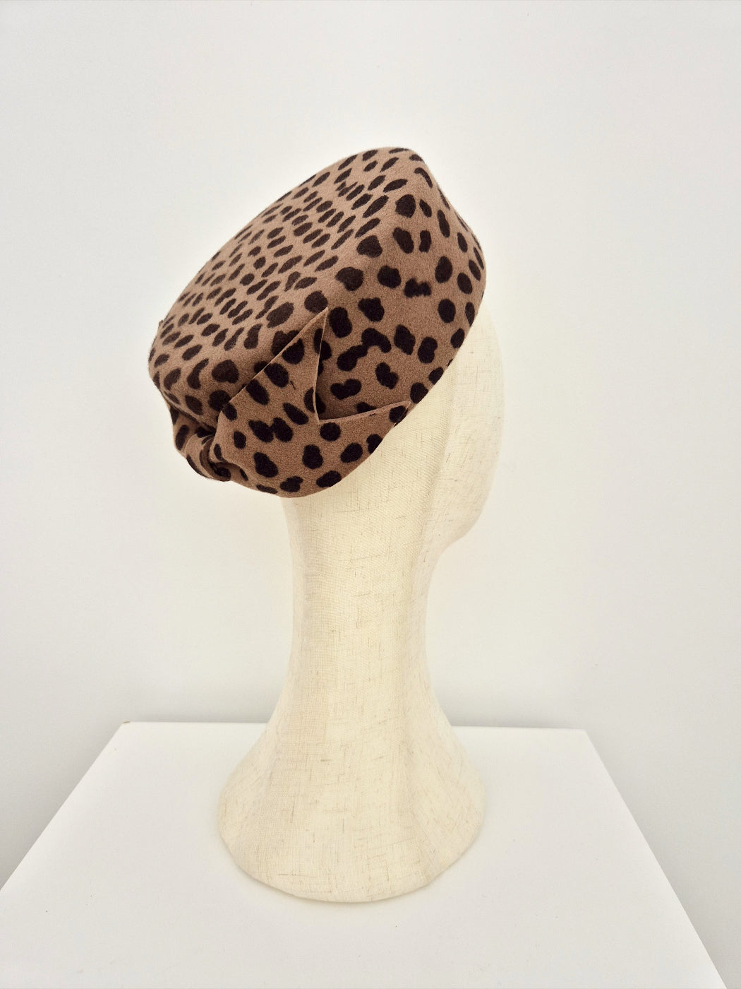 Leopard print pillbox headpiece on a mannequin head against a white background side back