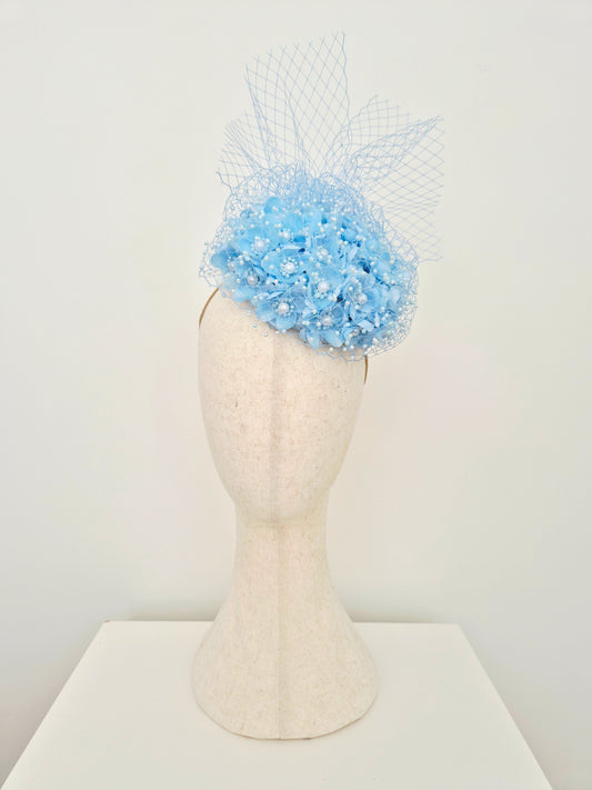 light blue 3d flower encrusted headpiece with veiling on a manniquin head against a white wall