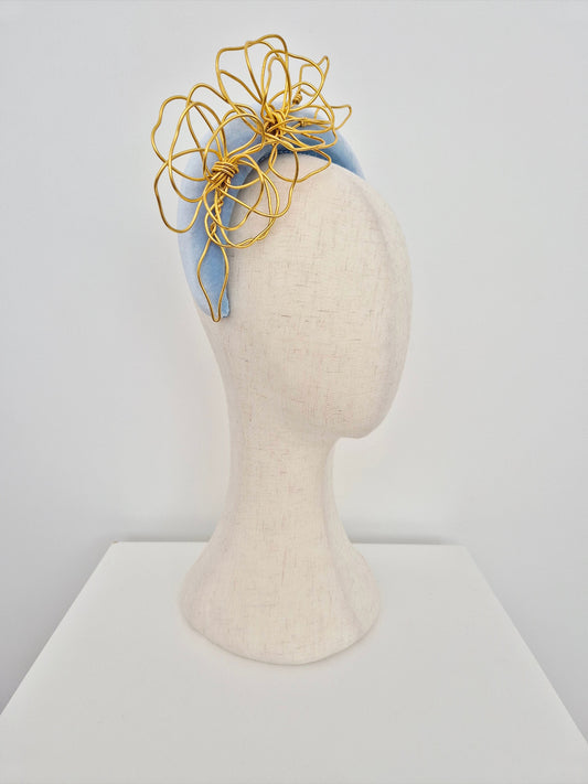 Mannequin head wearing a light blue headband with a gold floral accessory on a white background