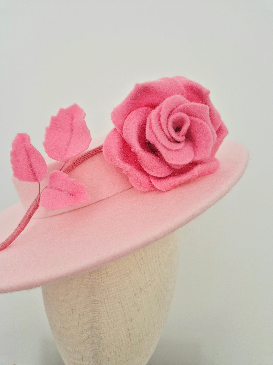 light Pink felt hat with pink rose floral decorations on a mannequin head against a white background close up