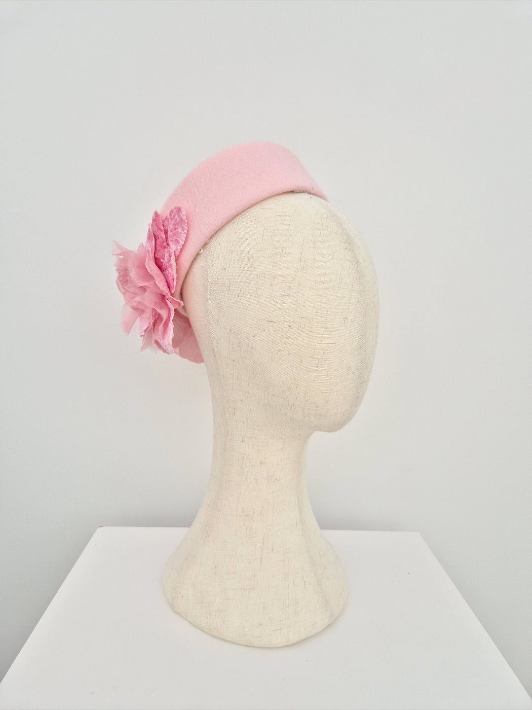 Pink pillbox headpiece with  flowers on a mannequin head against a white background side front