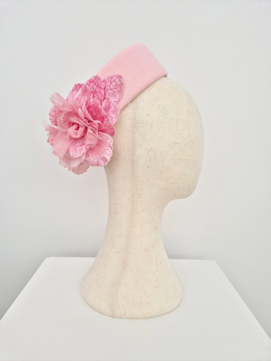 Pink pillbox headpiece with a large pink flower on a mannequin head against a white background side view