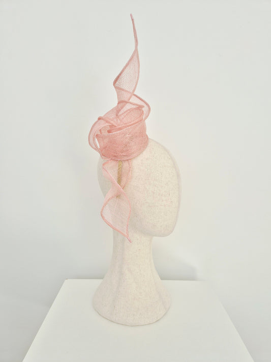 A light pink knot and tails straw fascinator an mannequin head, set against a plain white studio background. side view