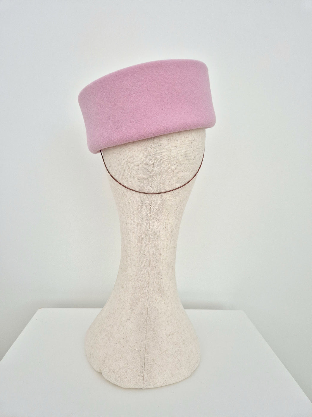 Pink felt wool pillbox hat on a mannequin head against a white background back view