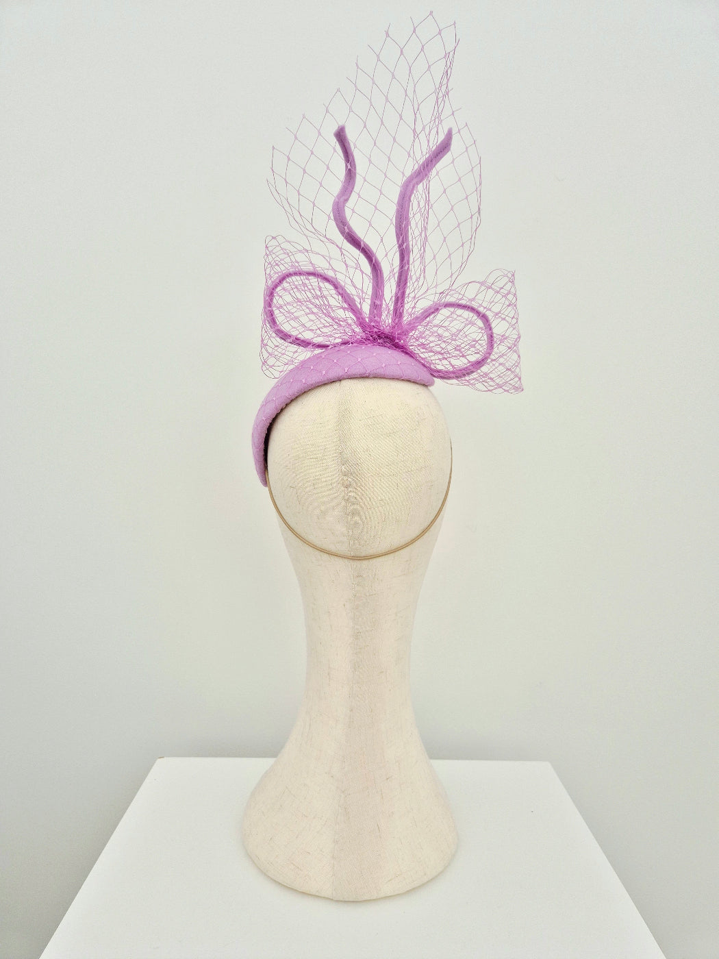lilac felt headpiece with decorative bow on a mannequin head against a white background back view