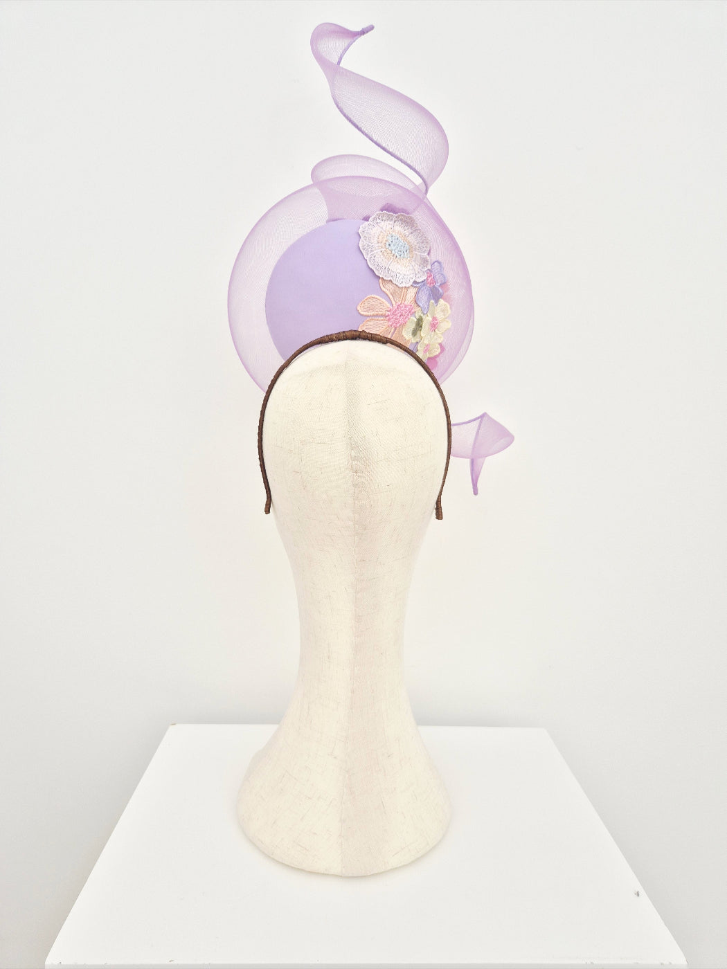 lilac percher headpiece with floral lace back view on a manniquin head against a white wall